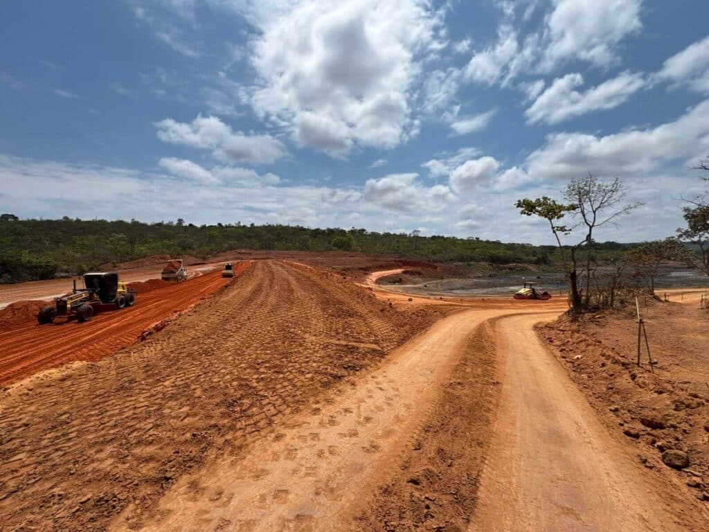 Fotografia aérea profissional de uma imensa barragem de terra e água finalizando etapas de contenção hidráulica.