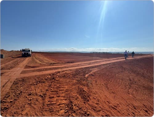 Visão aérea de maquinário pesado operando em solo preparado para contenção hídrica agrícola.